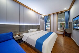 Habitación de hotel con una cama grande, una mesita de noche, una silla, un televisor y una ventana con cortinas.