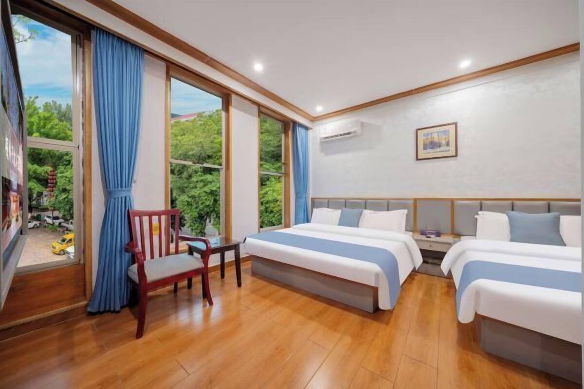 Ein Hotelzimmer mit zwei Betten, Holzboden, einem Sessel und großen Fenstern mit Vorhängen.