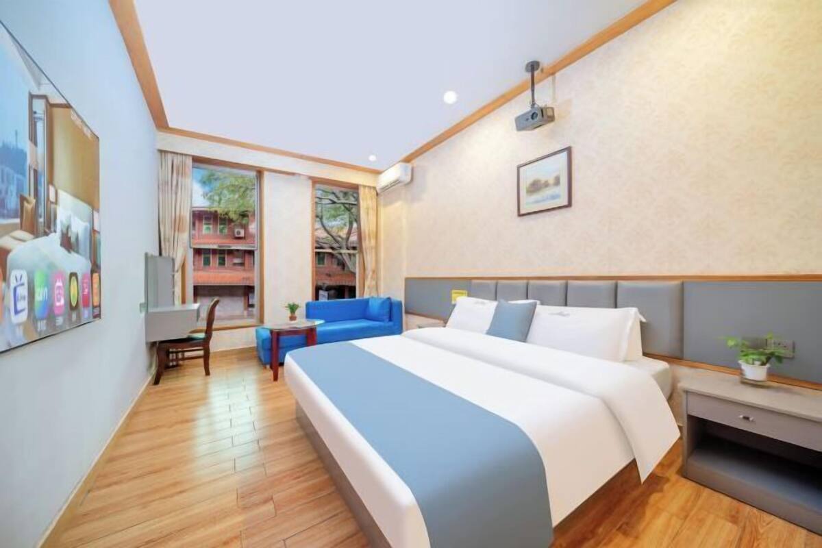 Ein Hotelzimmer mit einem großen Bett, einem blauen Sofa, einem kleinen Tisch und einem Fenster mit Blick auf Gebäude.
