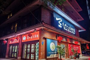 A traditional building with a sign for 'Ming Garden Hotel' and a large illuminated sign above the entrance. - Meizhou Tiandiren Garden Hotel (Meijiang Meixian People’s Square) (Meizhou)