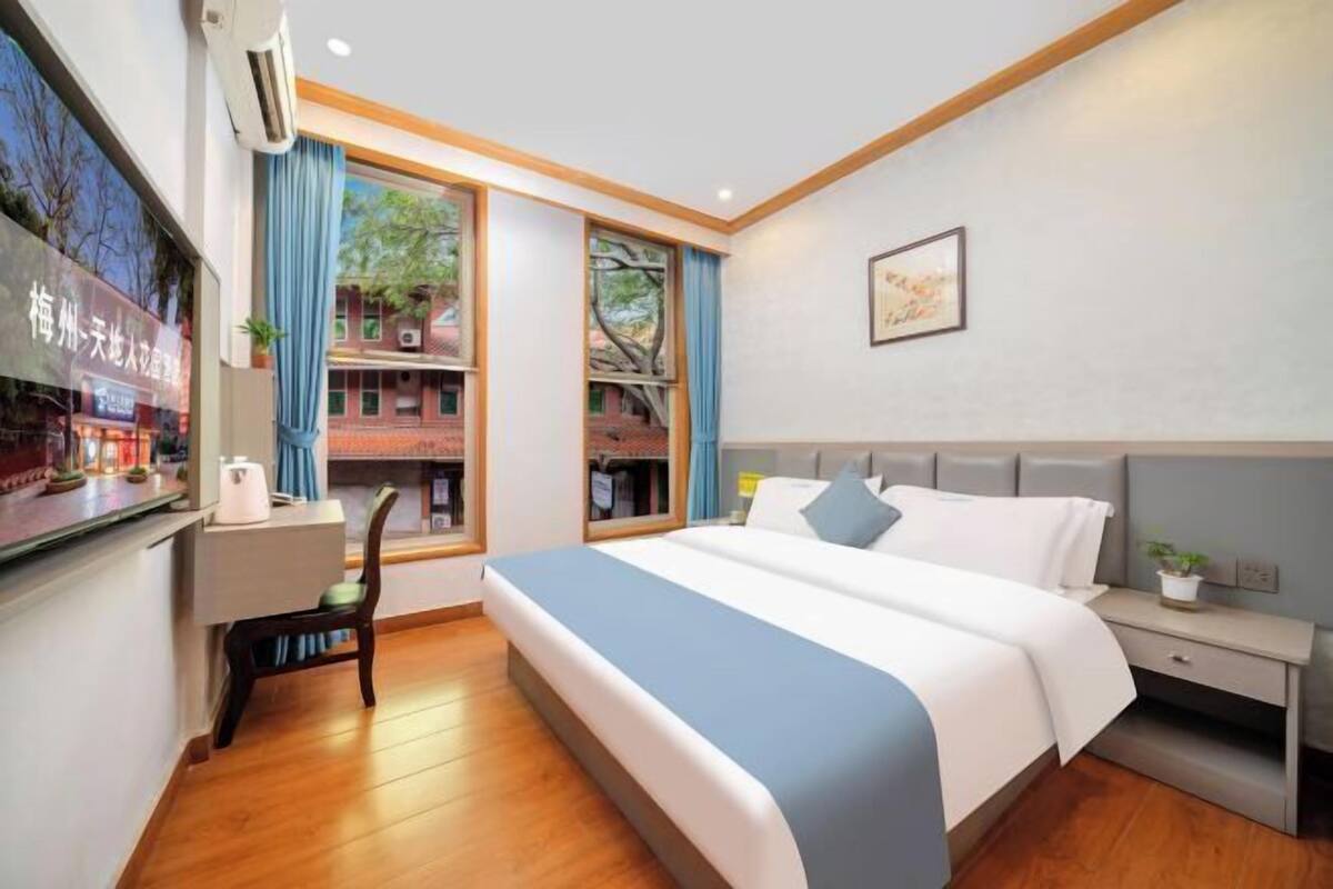 Ein Hotelzimmer mit Bett, Nachttisch, Stuhl und einem Fenster mit Blick auf ein Gebäude.
