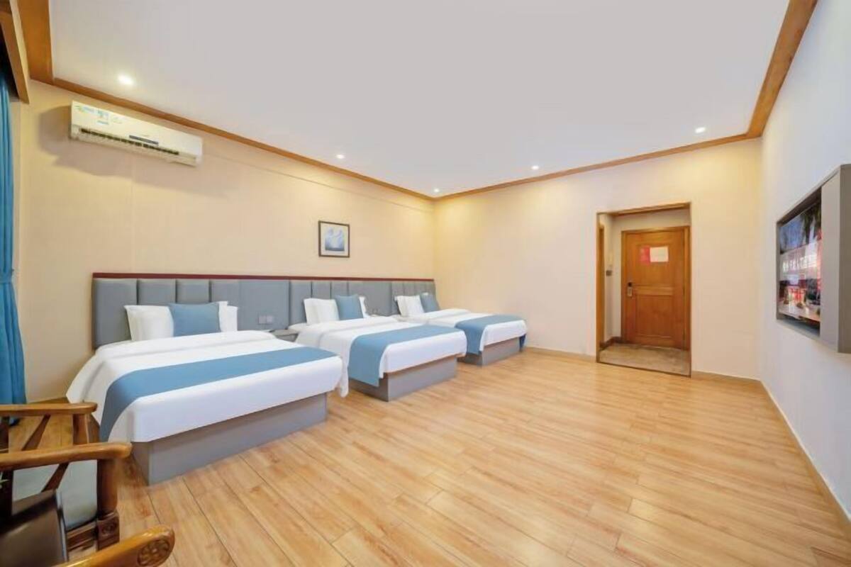 Ein Hotelzimmer mit drei Betten, Holzboden, einer Tür und einer Klimaanlage.