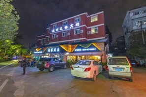 A multi-story building with a restaurant on the ground floor, several parked cars, and a parking lot. - Wenxie Hotel (Hangzhou)
