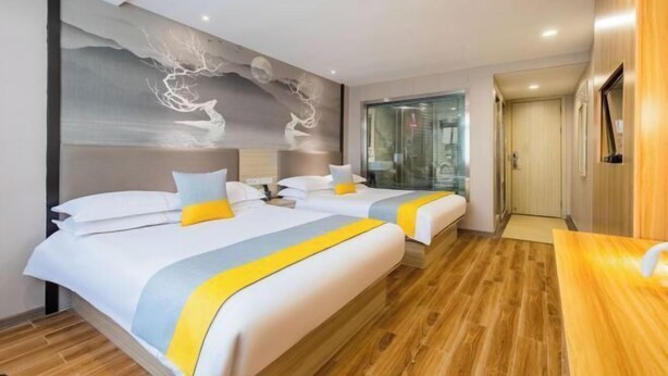 Ein Hotelzimmer mit zwei Betten, Holzboden, Wandgemälde und Fernseher.