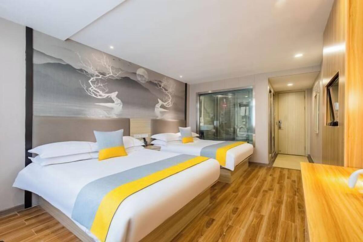 Habitació d'hotel amb dos llits, un terra de fusta, un mural a la paret i un televisor.
