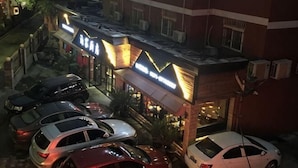 Ein Hotel mit mehreren parkenden Autos vor der Fassade, einem gut beleuchteten Eingang und einer sichtbaren Klimaanlage an der Außenwand.