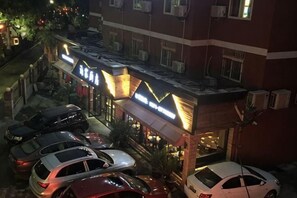 Een hotel met meerdere auto's voor de gevel, een goed verlichte ingang en een zichtbare airconditioning.