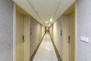 Een hotelgang met deuren aan beide kanten, een marmeren vloer en een lichtkleurig plafond.