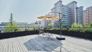 Eine Dachterrasse mit Tisch und Stühlen, einem Sonnenschirm und Blick auf hohe Gebäude.