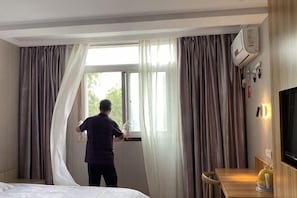 A hotel room with a bed, a window with curtains, a television, and a desk with a lamp. - Wenxie Hotel (Hangzhou)