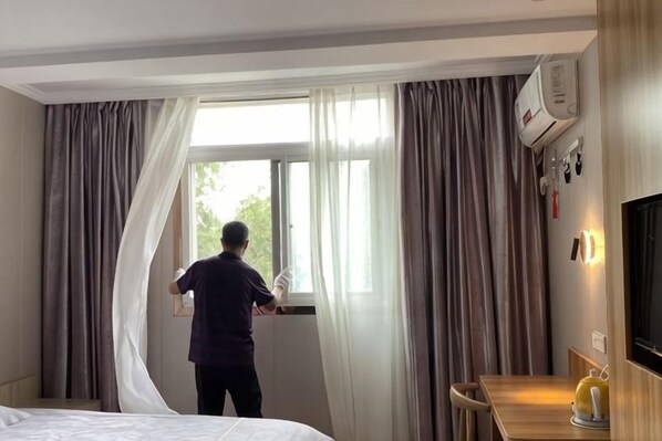 A hotel room with a bed, a window with curtains, a television, and a desk with a lamp. - Wenxie Hotel (Hangzhou)
