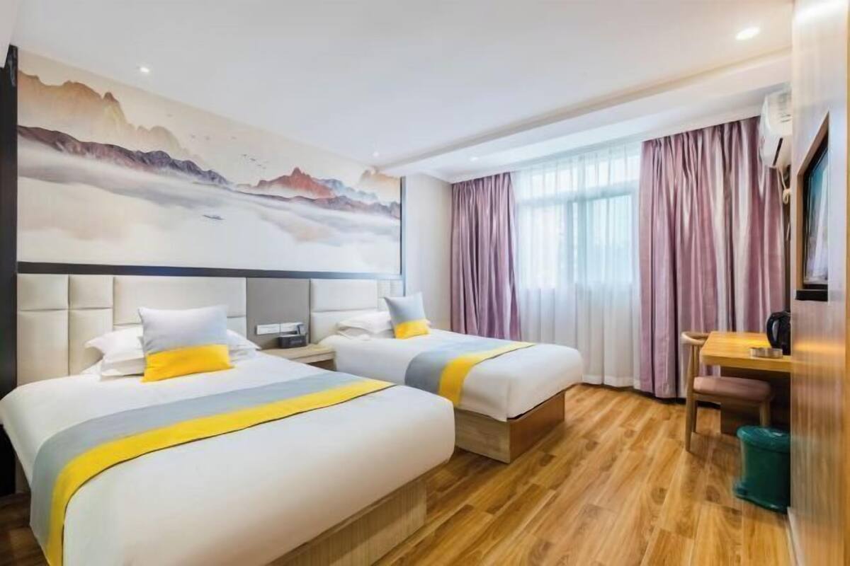 Habitació d'hotel amb dos llits, un sòl de fusta, un quadre gran a la paret i una finestra amb cortines.