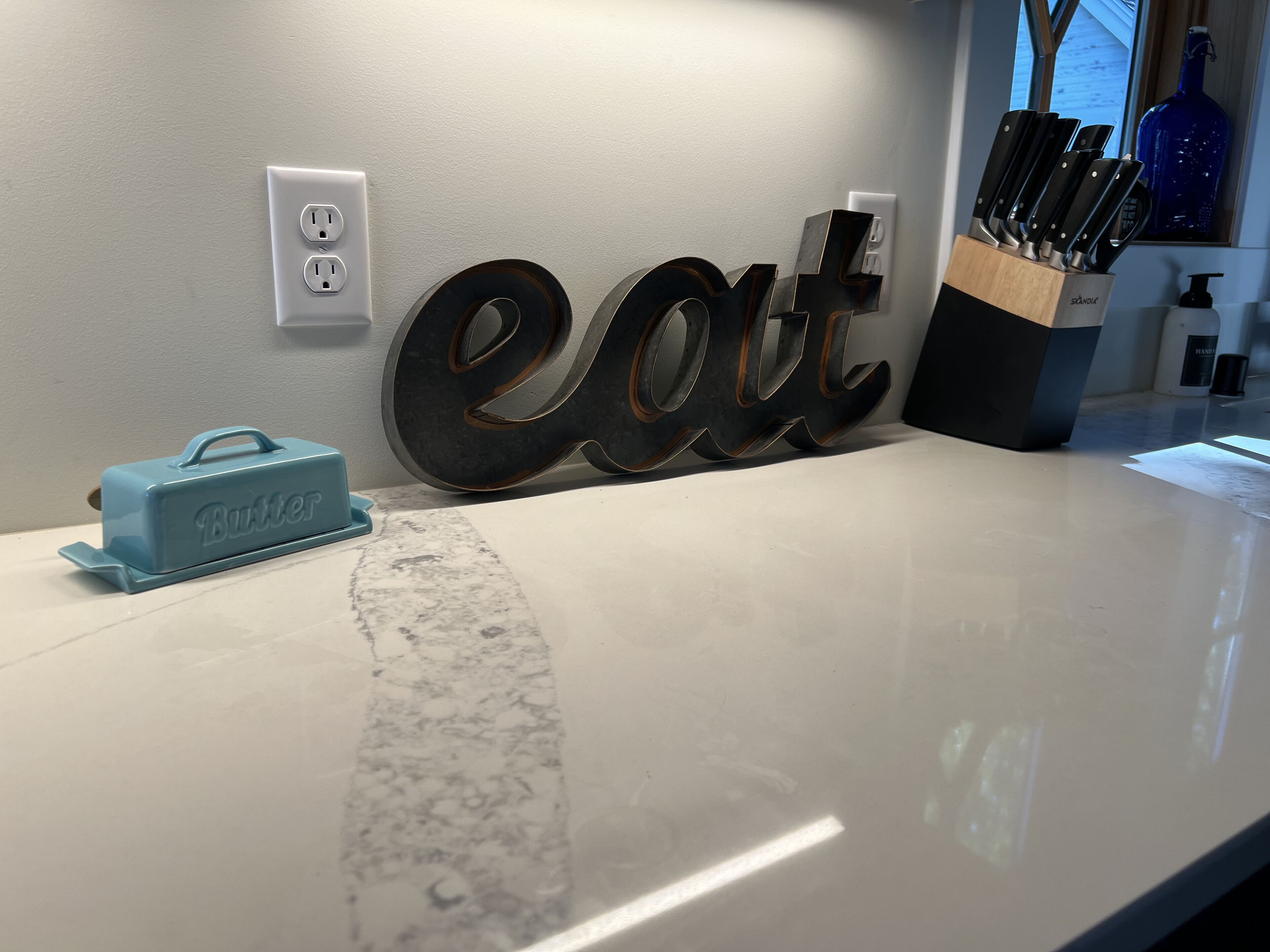 Una encimera de cocina con un letrero que dice 'eat', un portalápices para cuchillos de mantequilla y un cuchillo para mantequilla.
