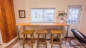 Eine Küche mit Holzausziehtisch, drei Barhocker, einer Heizung und einem Fenster mit Jalousien.