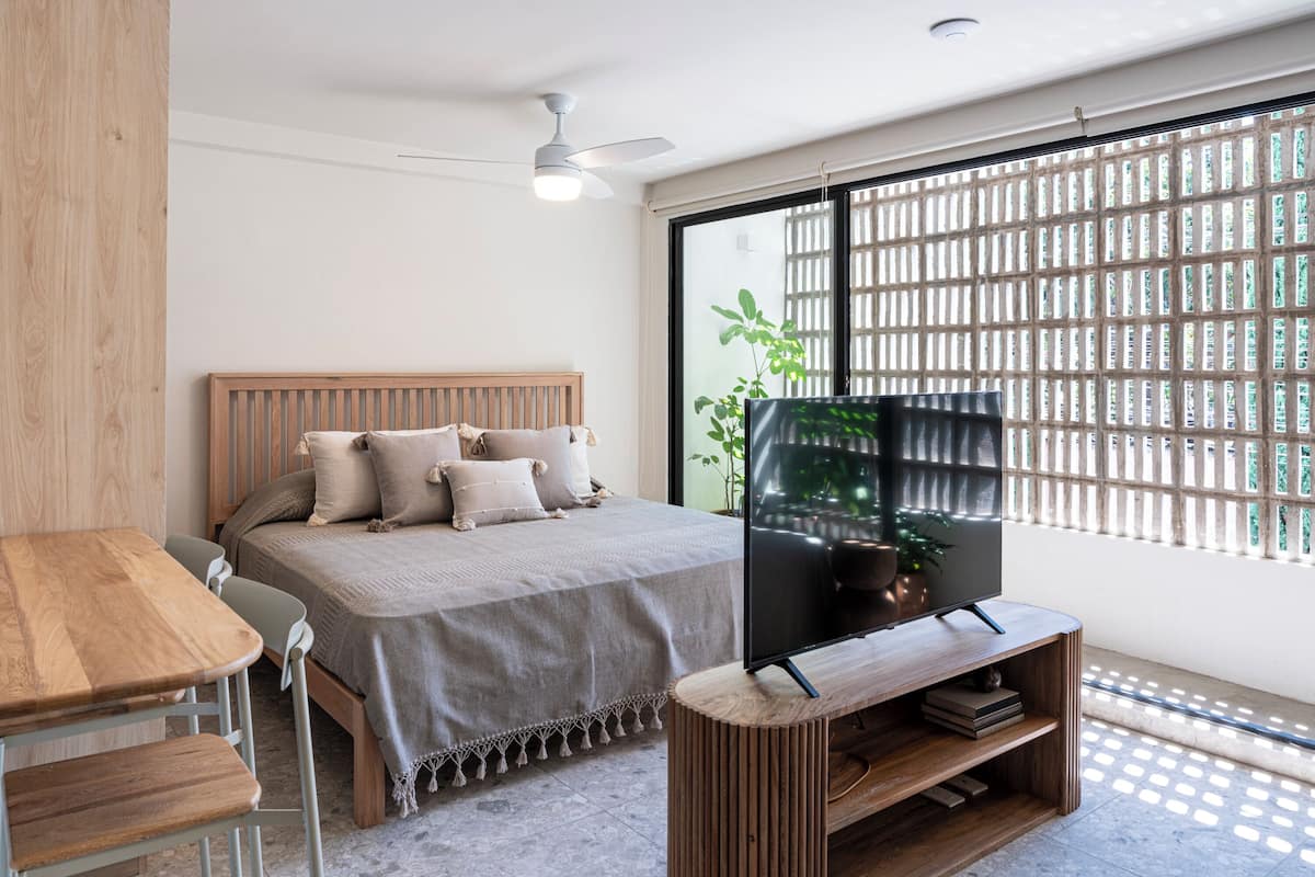 Ein Schlafzimmer mit einem Bett, einem Fernseher auf einem Holzständer, einem Deckenventilator und einem Fenster mit Gittermuster.