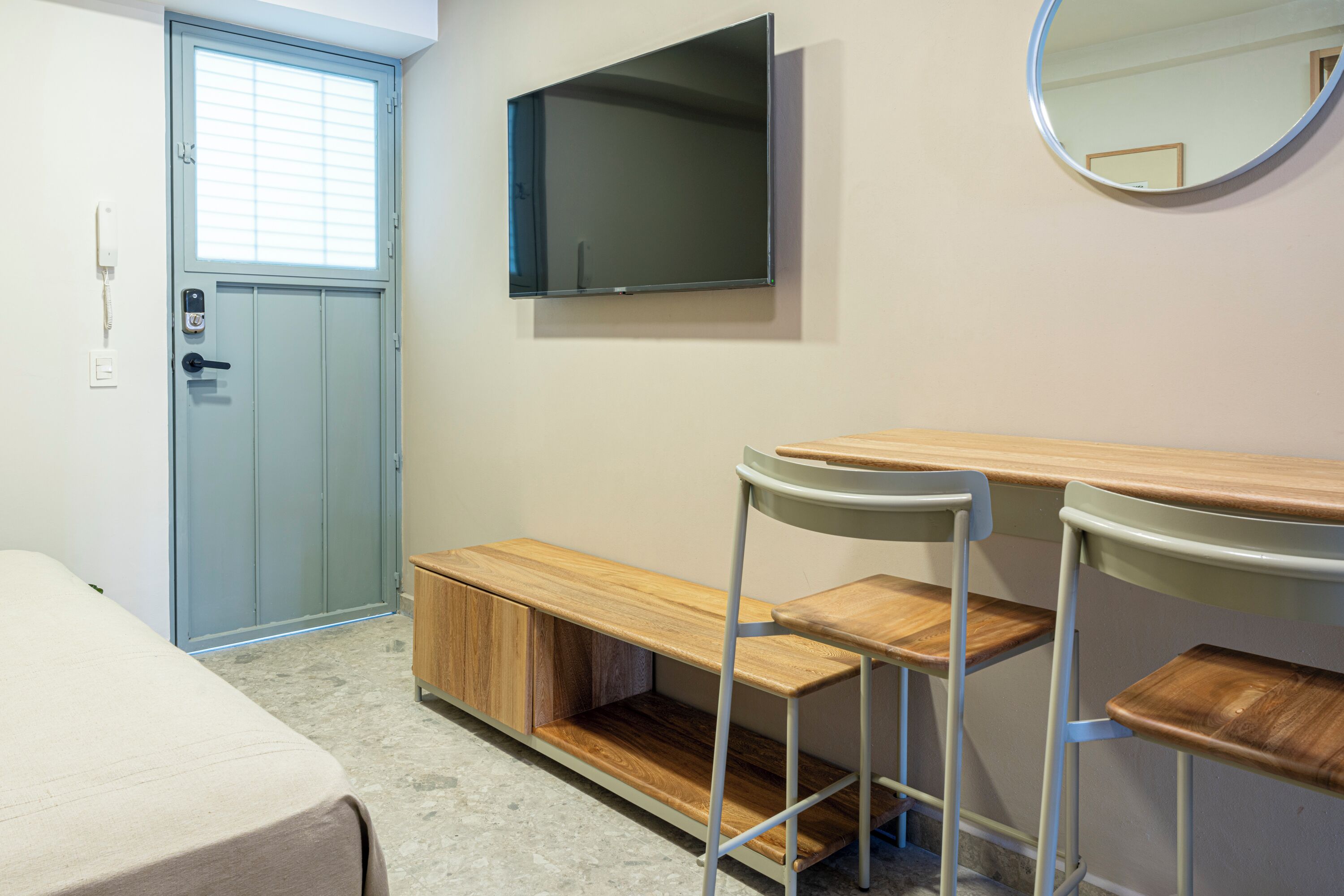 Una habitación con una cama, un escritorio con dos sillas, un televisor y un espejo en la pared.