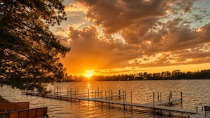 A lakeside view with a wooden dock, a bench, and a sunset.