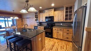 A kitchen with wooden cabinets, a stainless steel refrigerator, a central island with stools, and a built-in oven.