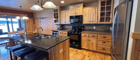 A kitchen with wooden cabinets, a stainless steel refrigerator, a central island with stools, and a built-in oven.