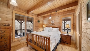 Quarto de cabana de madeira com uma cama de madeira, duas mesas de cabeceira, um aparador e janelas amplas.