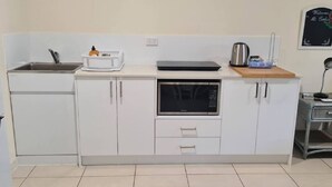 A compact kitchen with white cabinets, a built-in microwave, a sink, and a small countertop with a kettle and a laptop. - Mountain Views beside the Seaside. (Mount Coolum)