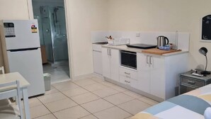 A compact hotel room with a kitchenette, a bed, a small table, and a shower area. - Mountain Views beside the Seaside. (Mount Coolum)