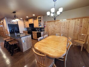 A kitchen with wooden cabinets, a central island, and a dining area with wooden chairs. - Lakefront Home on the Whitefish Chain - Outdoor Pool, Pickleball Courts and More (Pequot Lakes)