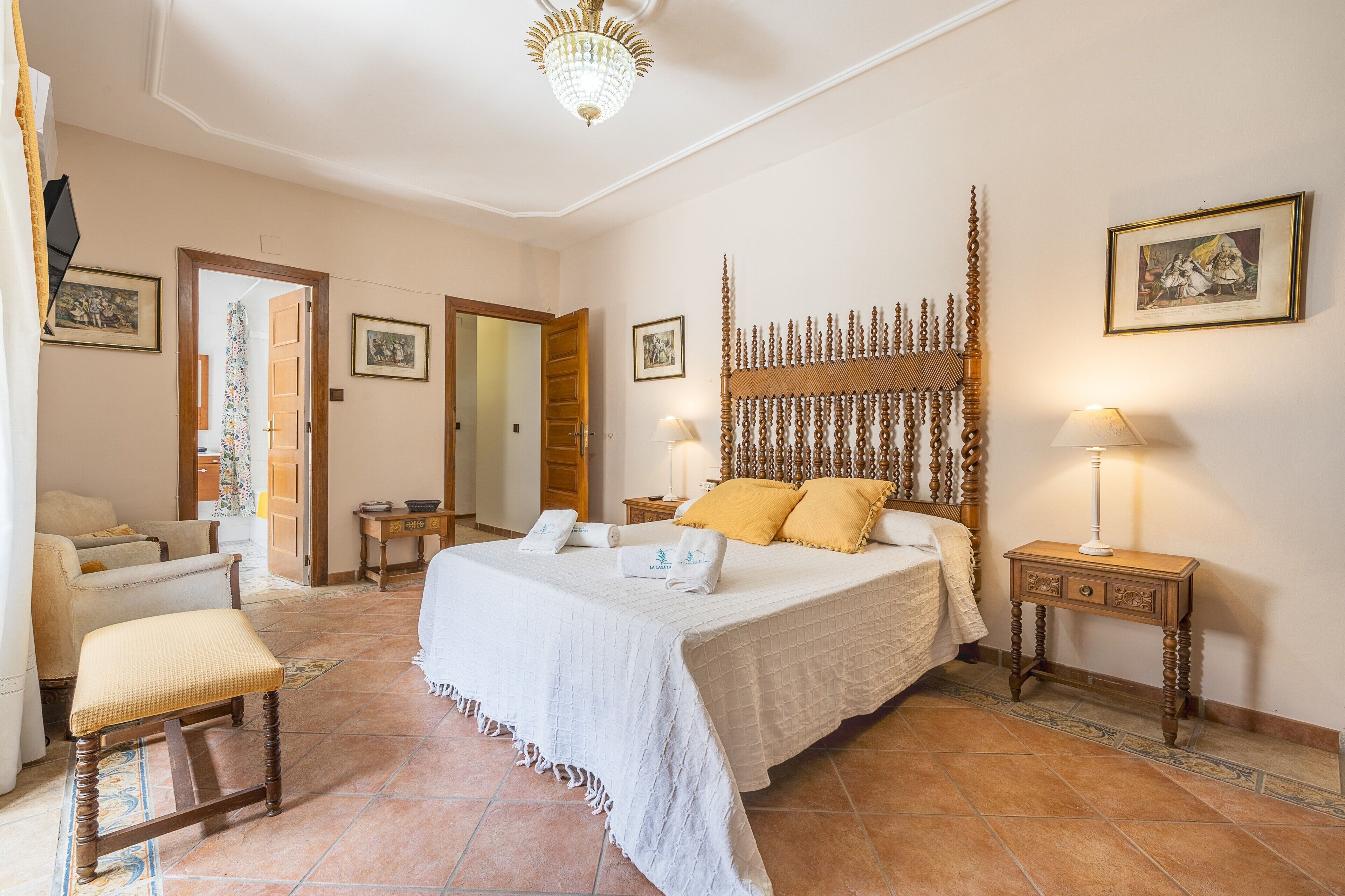 Un dormitorio espacioso con una cama grande, una zona de estar con una silla, un cabecero de madera y una mesita de noche con una lámpara.