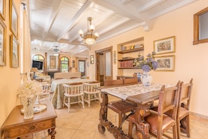 Un coin repas avec une table en bois, des chaises et un lustre. On y trouve également des étagères et des tableaux encadrés accrochés aux murs.