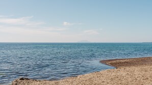A beach with calm water, a rocky shoreline, and a distant mountain.