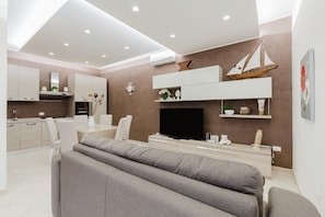 Ein modernes Wohnzimmer mit Flachbildfernseher, grauen Sofas, einer Küchenzeile und einer aufgehängten Bootsdekoration.