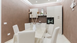 A modern dining area with a table set for four, white chairs, and a vase with decorative branches.