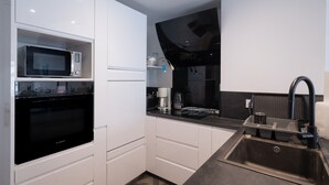 Una cocina moderna con armarios blancos, un horno Bosch, microondas, encimera negra, un lavamanos con grifo y una cafetera.
