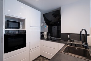 A modern kitchen with white cabinetry, a Bosch oven, a microwave, a black countertop, a sink with a faucet, and a coffee maker.