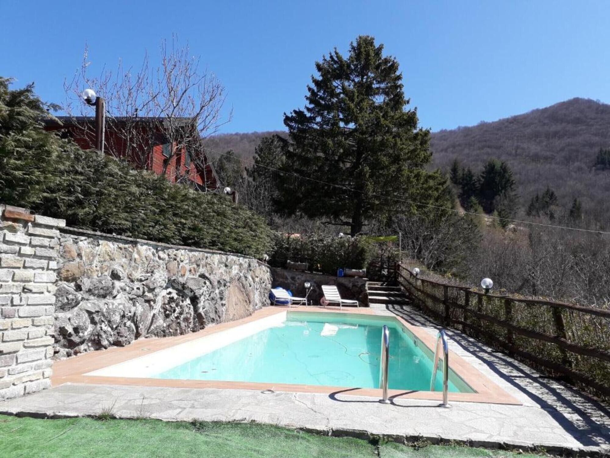 Una piscina con un muro de piedra, una terraza de madera y vistas a la montaña.