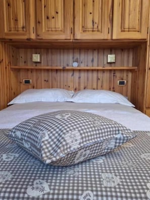 A wooden-paneled room with a bed, pillows, and a checkered bedspread.