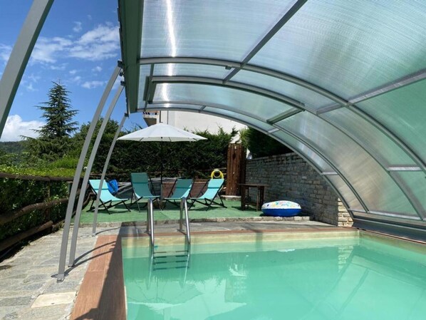 A swimming pool with a glass enclosure, lounge chairs, and a small inflatable float.