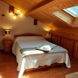 A bedroom with a wooden ceiling, a skylight, a bed with a white bedspread, and two bedside lamps. - Room 'Primula' with Mountain View, Shared Pool and Wi-Fi (Santo Stefano d'Aveto)