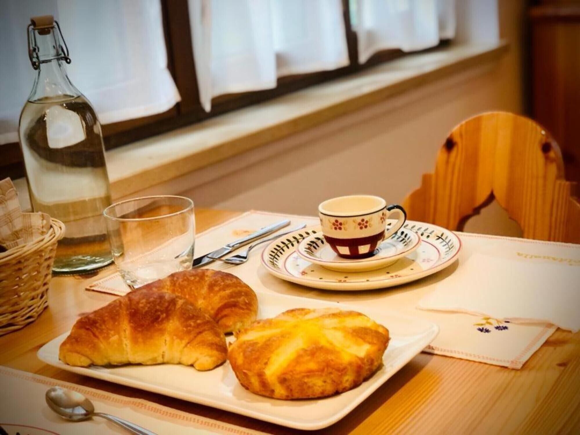 A breakfast setting with croissants, a cup of coffee, and a bottle of water on a table.