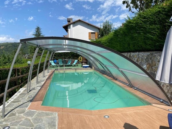 Une piscine dotée d’une enceinte en verre, entourée d’un revêtement de sol en pierre, et offrant une vue sur une montagne et une maison en arrière-plan.