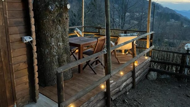 Una terraza de madera con una mesa y sillas, rodeada por una valla de madera, con vistas a un paisaje montañoso.