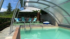 Una piscina con cerramiento de vidrio, sillas de descanso y un flotador inflable pequeño.