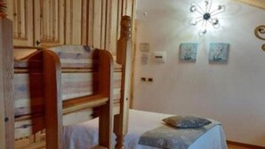 Una cama litera de madera con colcha blanca, una lámpara fijada a la pared y dos cuadros enmarcados.