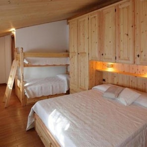 Une chambre avec un lit superposé en bois, une échelle en bois, un lit simple et des armoires encastrées en bois.