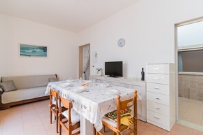Ruokailutila, jossa on kahdelle katettu pöytä, sohva, televisio ja kaappi.