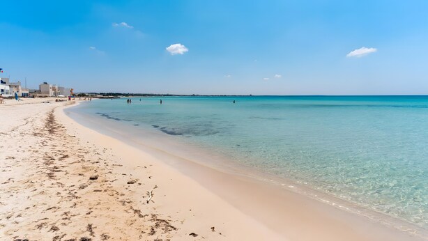 Une plage avec une eau cristalline, un rivage sablonneux et des bâtiments en arrière-plan.