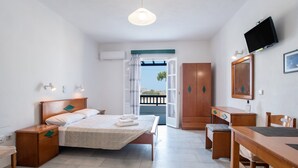 A bedroom with a bed, bedside tables, a desk, a chair, a television, and a view through an open door.