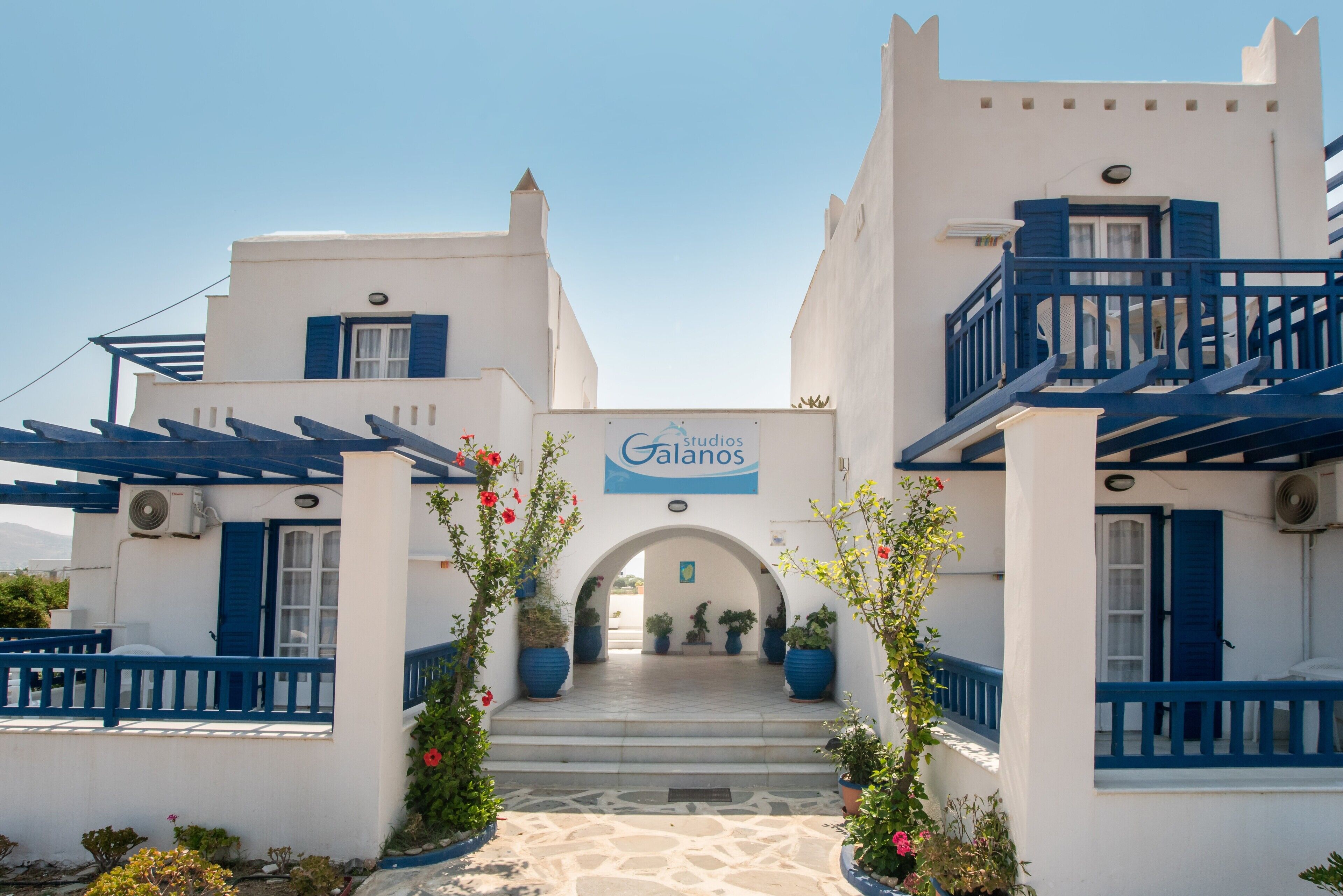 A building with a sign reading 'Galanos,' a white facade with blue accents, and a stone-paved entrance.