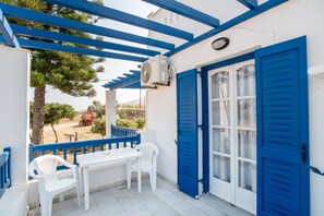 Un balcón con una mesa y sillas blancas, contraventanas azules y un equipo de aire acondicionado.