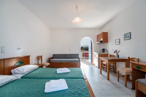 A hotel room with two beds, a sofa, a dining table with chairs, a wooden cabinet, and a view through an arched doorway. - Studio Apartment '4' with Sea View, Wi-Fi and Air Conditioning (Naxos Chora)